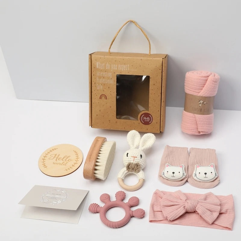 Collection of baby items including a box, blanket, teether, and toys on a white background