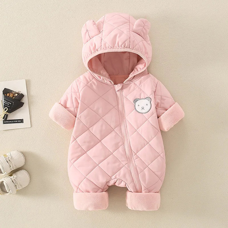 Pink quilted baby snowsuit with bear patch on a beige background