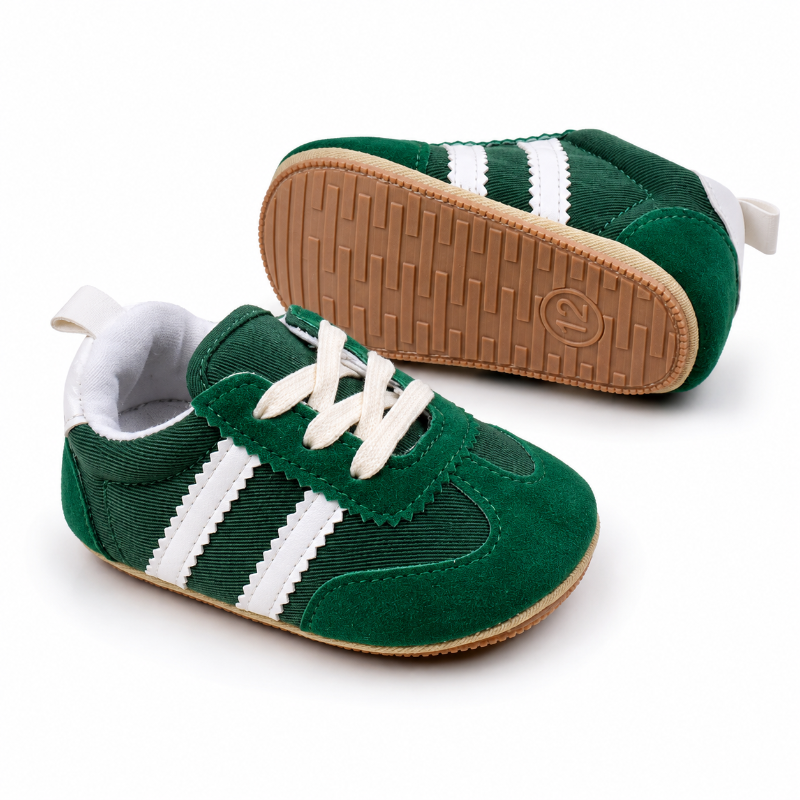 A pair of green baby sneakers with white stripes and white laces, shown on a clean white background. One shoe is positioned to show the side profile, and the other is angled to show the brown textured rubber sole.