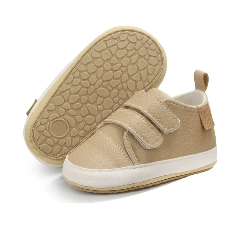 A pair of beige baby sneakers with hook and loop closure and a non-slip sole, designed for comfort and ease of wear for young children.