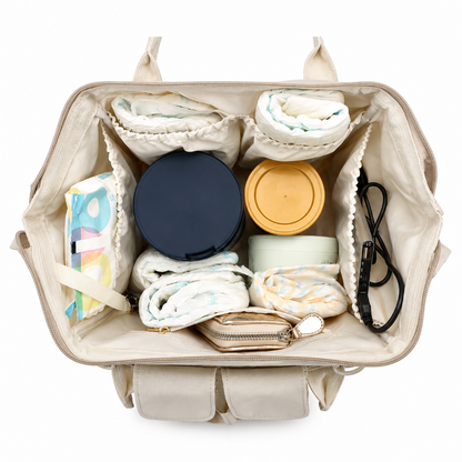 An open beige diaper bag shown from above, packed with baby essentials including folded diapers, a dark blue round container, a yellow-lidded jar, a small pouch, wipes, and a black cord on a white background.