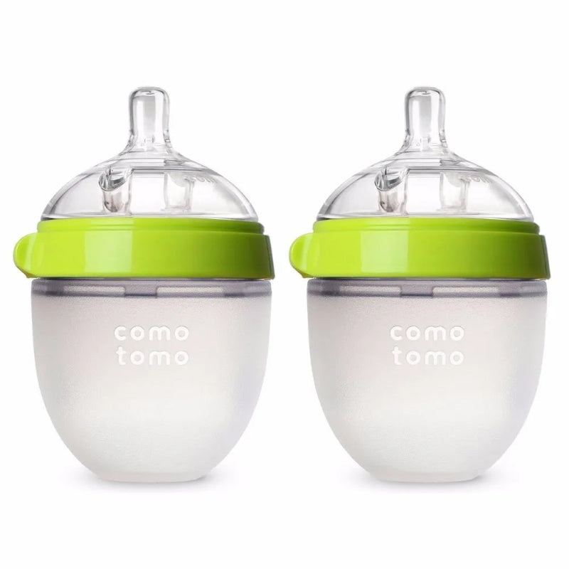 Two silicone baby bottles with wide necks and colorful tops, one pink and one green, on a light background.