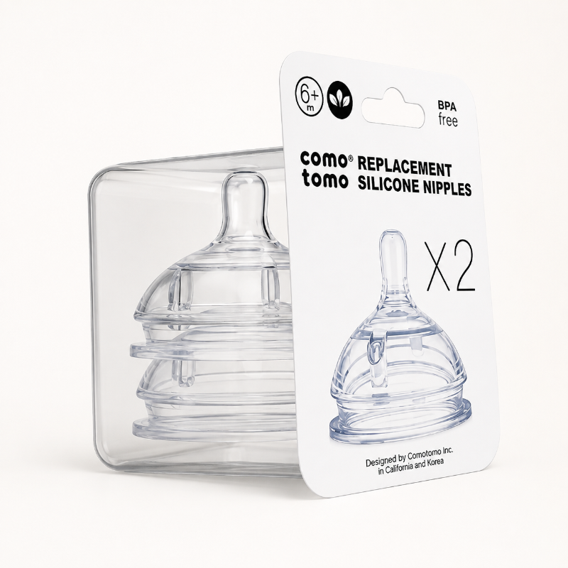 Two clear silicone baby replacement nipples in a transparent plastic case with a white retail card labeled 'como tomo replacement silicone nipples x2' on a light neutral background.
