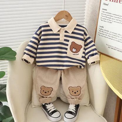 A set of baby boy clothing featuring a striped green and beige polo shirt with a bear cartoon design, paired with beige pants with bear patches, displayed on a mannequin.