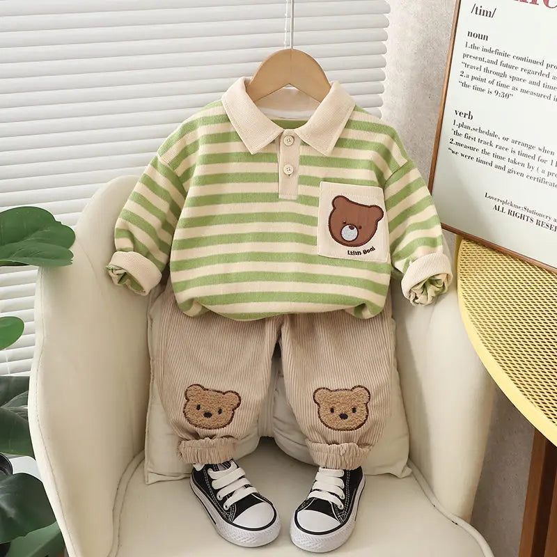 A set of baby boy clothing featuring a striped green and beige polo shirt with a bear cartoon design, paired with beige pants with bear patches, displayed on a mannequin.