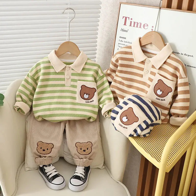 A set of baby boy clothing featuring a striped green and beige polo shirt with a bear cartoon design, paired with beige pants with bear patches, displayed on a mannequin.