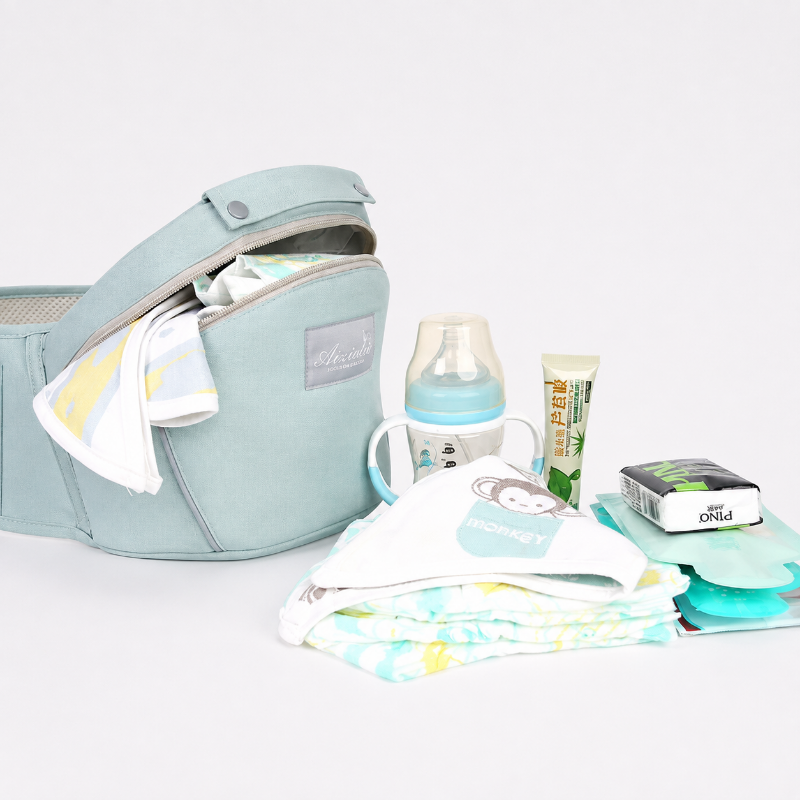 A light blue baby diaper bag shown open with baby accessories arranged beside it, including a bottle with a cup, a tube, wipes, and folded cloths. The setup is photographed on a clean white studio background.