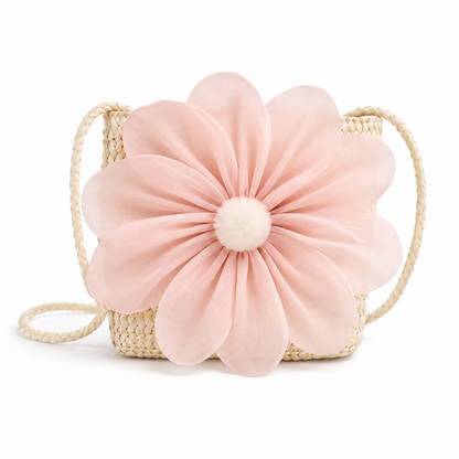 A woven straw shoulder bag featuring a large, pleated light pink fabric flower with a white pom-pom center, set against a plain white background.