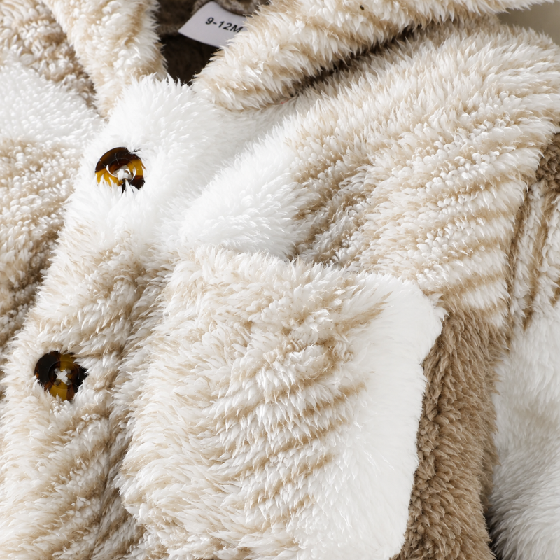 Close-up of a plush teddy-style jacket in cream and taupe tones, showing the soft textured fabric, a white pocket flap, and tortoiseshell-style buttons.