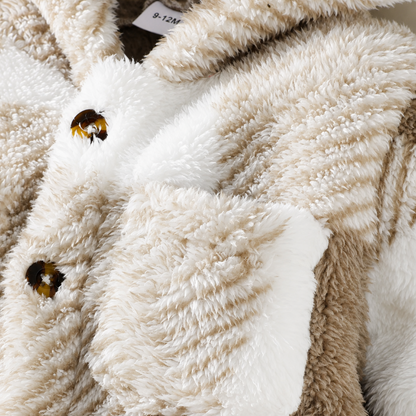 Close-up of a plush teddy-style jacket in cream and taupe tones, showing the soft textured fabric, a white pocket flap, and tortoiseshell-style buttons.