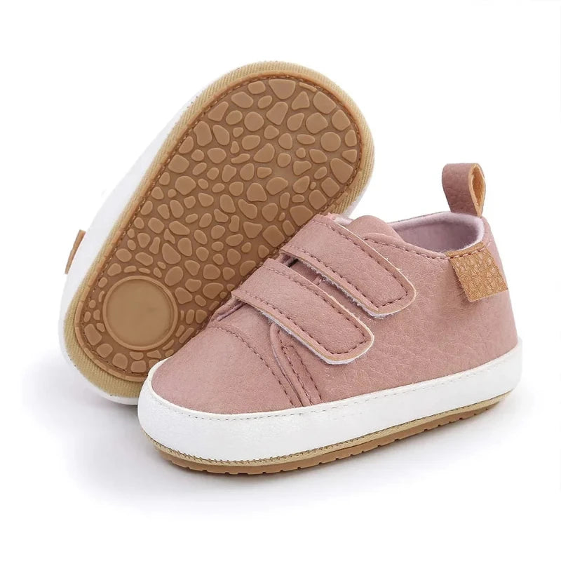 A pair of beige baby sneakers with hook and loop closure and a non-slip sole, designed for comfort and ease of wear for young children.